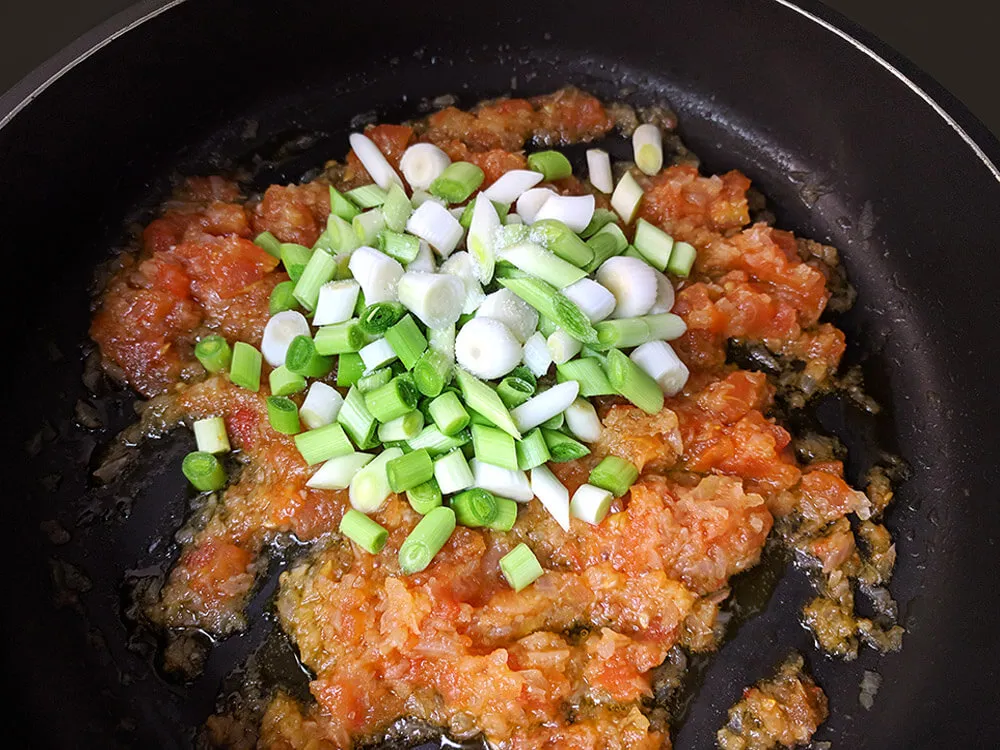 Cebolla pochada con tomate a dados y ajos tiernos.