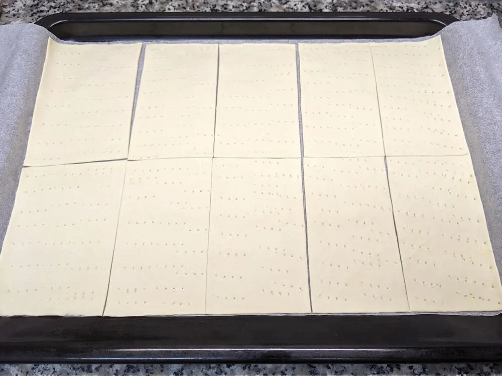 Masa de hojaldre fresca cortada a rectángulos, pinchada con un tenedor.
