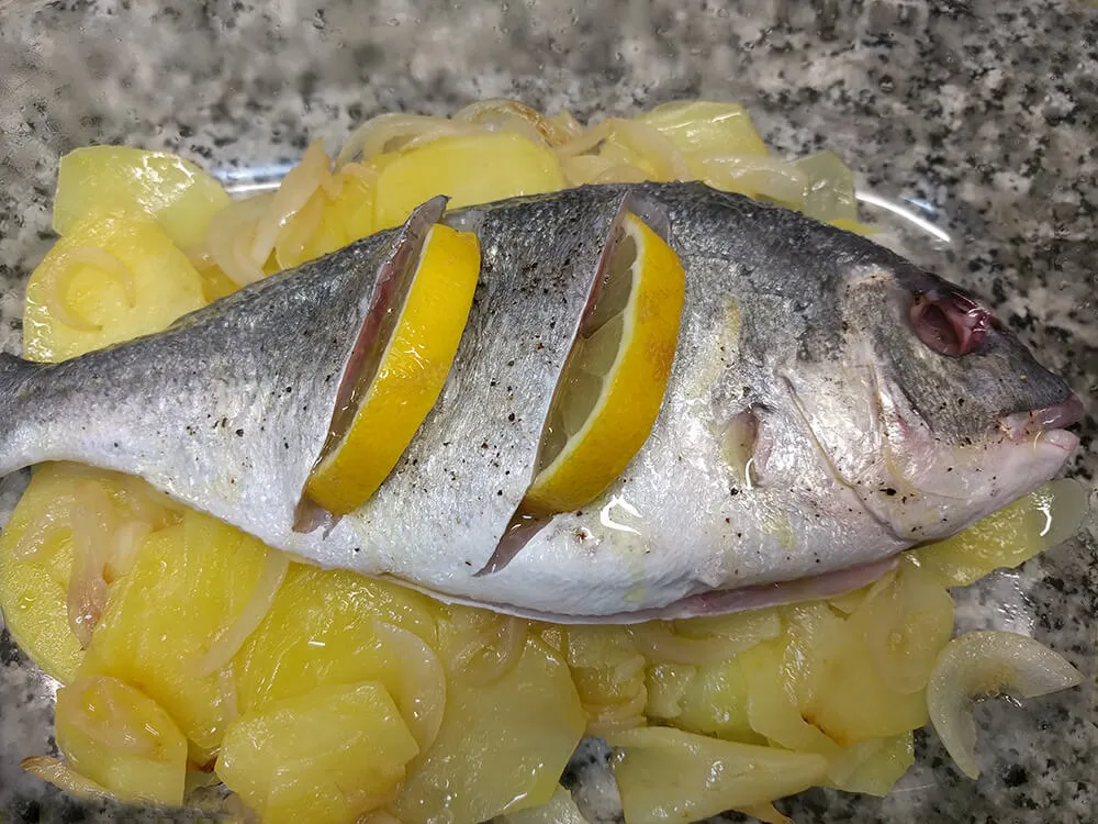 Dorada con las patatas y la cebolla en la fuente del horno