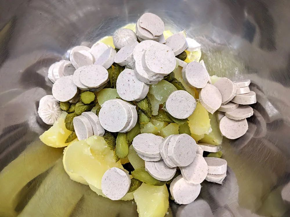 Patatas cocidas cortadas, pepinillos y bratwurst cortados.