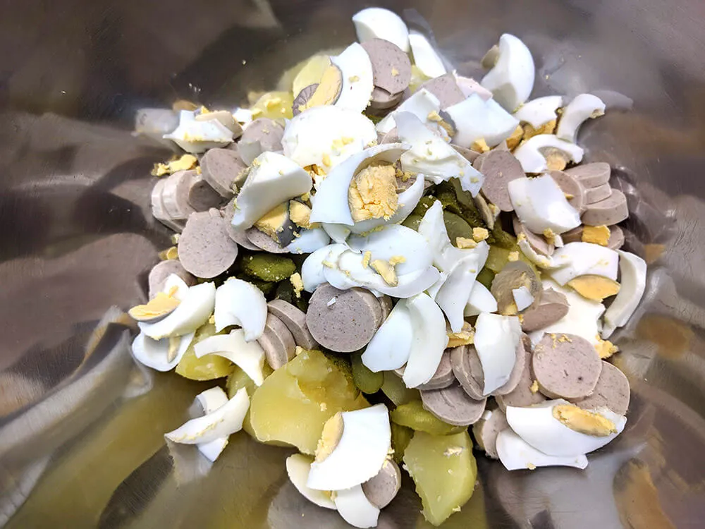 Patatas cocidas cortadas, pepinillos, bratwurst y huevo cocido cortados.