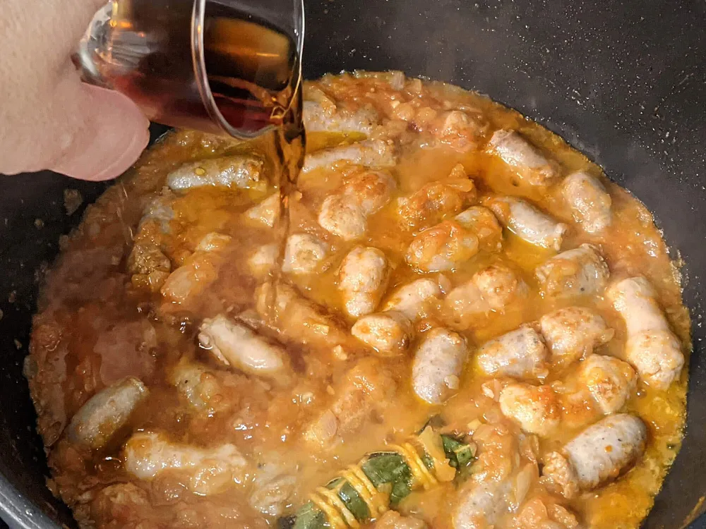 Sofrito de cebolla y tomate con salchichas y vino.