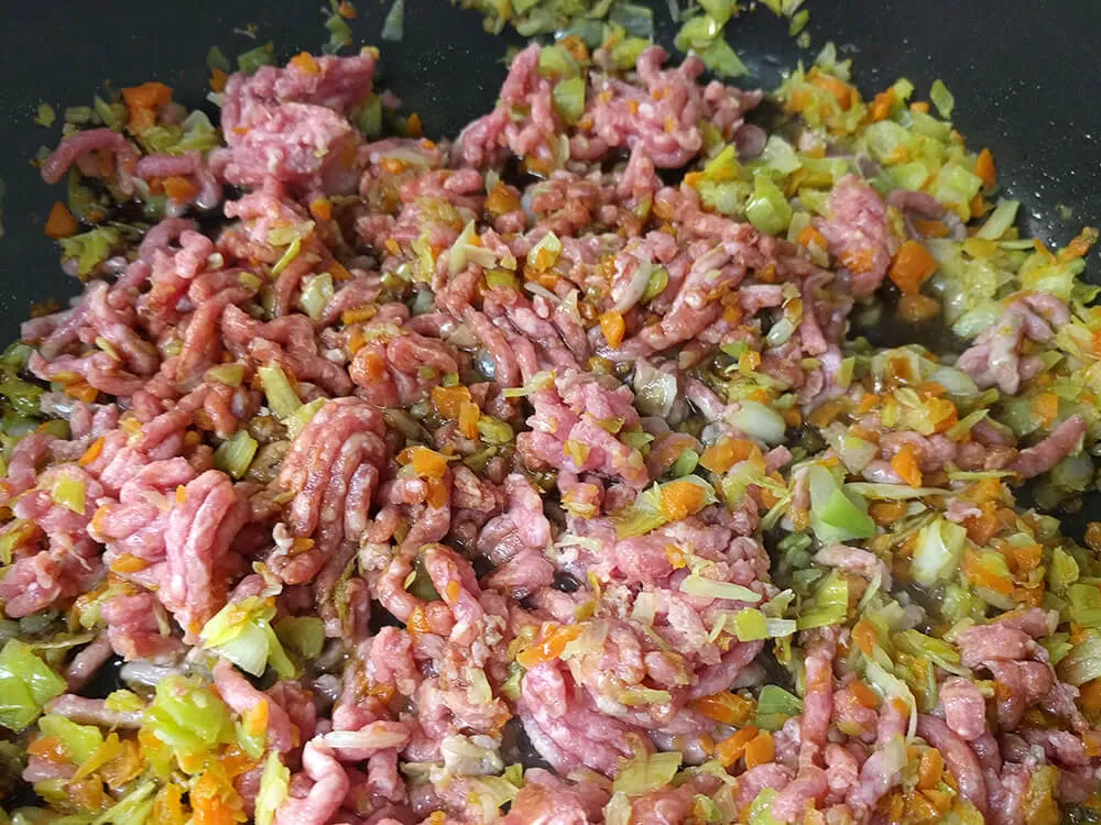 Mezcla carne picada con el puerro y la zanahoria cocinándose