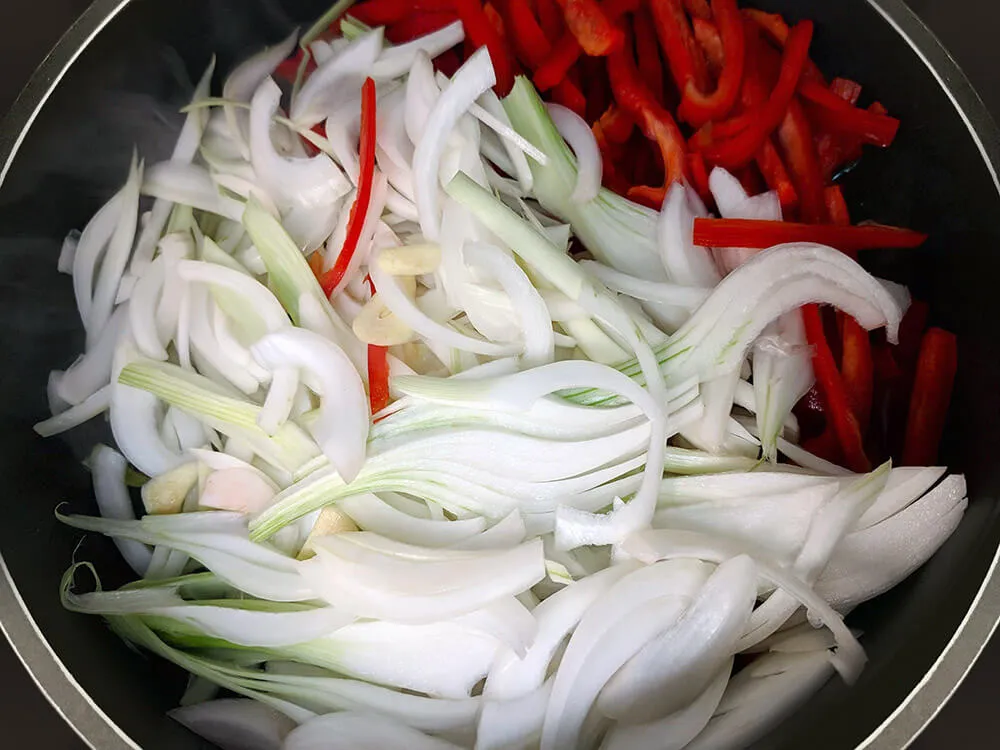 Cazuela con pimiento, cebolla y dientes de ajo cortados.