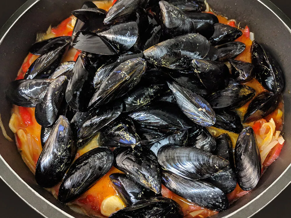 Cazuela con pimiento, cebolla, dientes de ajo, tomate cortados y mejillones.