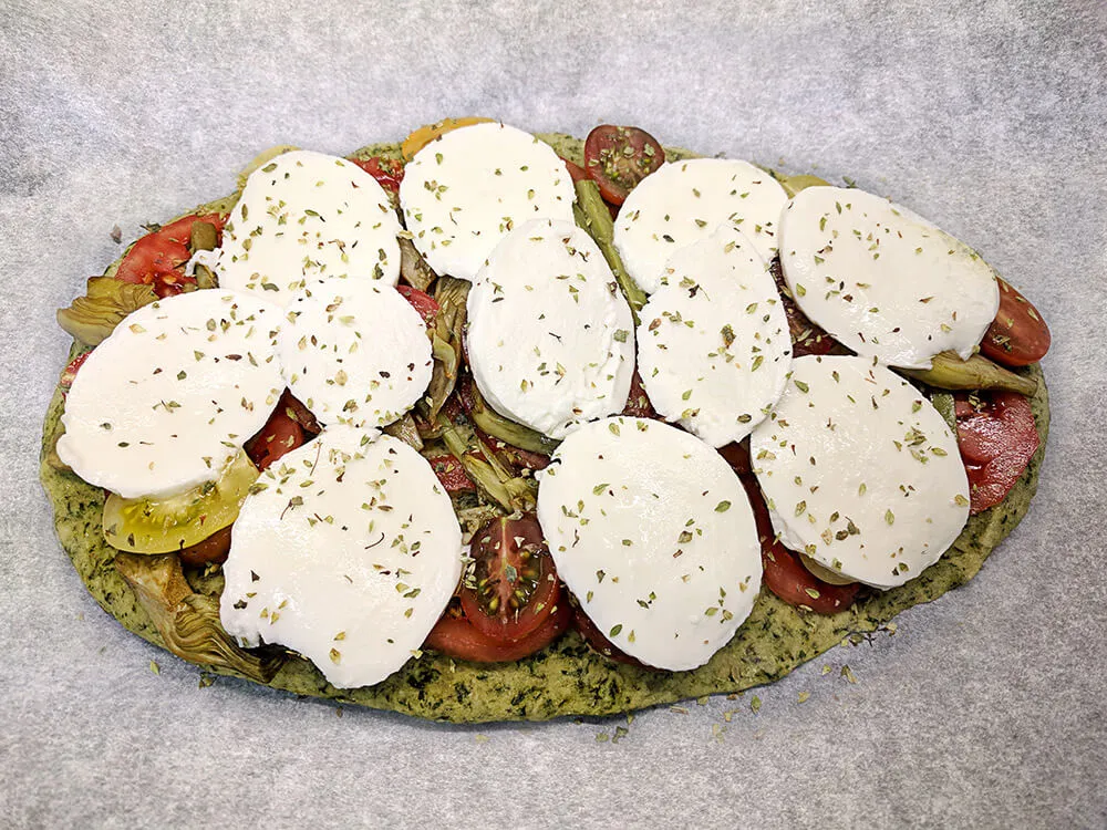 Pan kale con rodajas de tomate de pera, alcachofas, cherry y mozzarella sin lactosa.