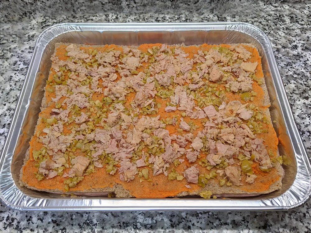 Capa de pan de molde, tomate triturado, atún y olivas picadas.