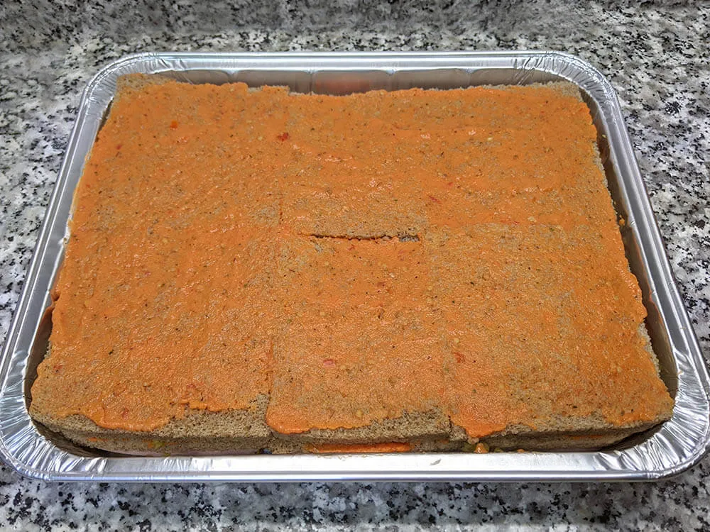 Capa de pan de molde untado con tomate triturado.