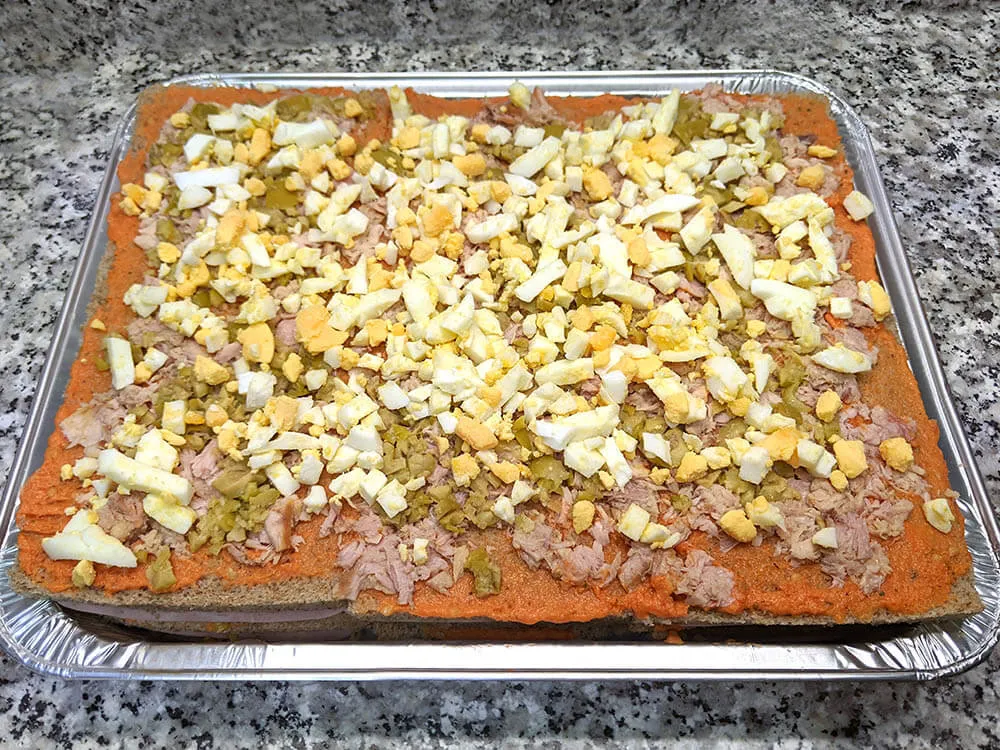 Capa de pan de molde, tomate triturado, atún, olivas picadas y huevo duro.