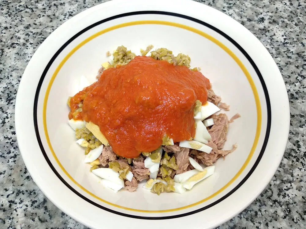 Cuenco con atún, huevos cocidos picados, olivas picadas y sofrito casero.