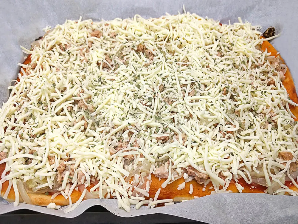 Base de pizza con cebolla frita, atún, mozzarella y orégano.