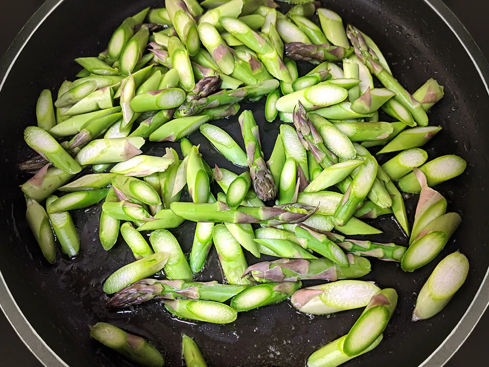 Espárragos tiernos cortados rehogándose.