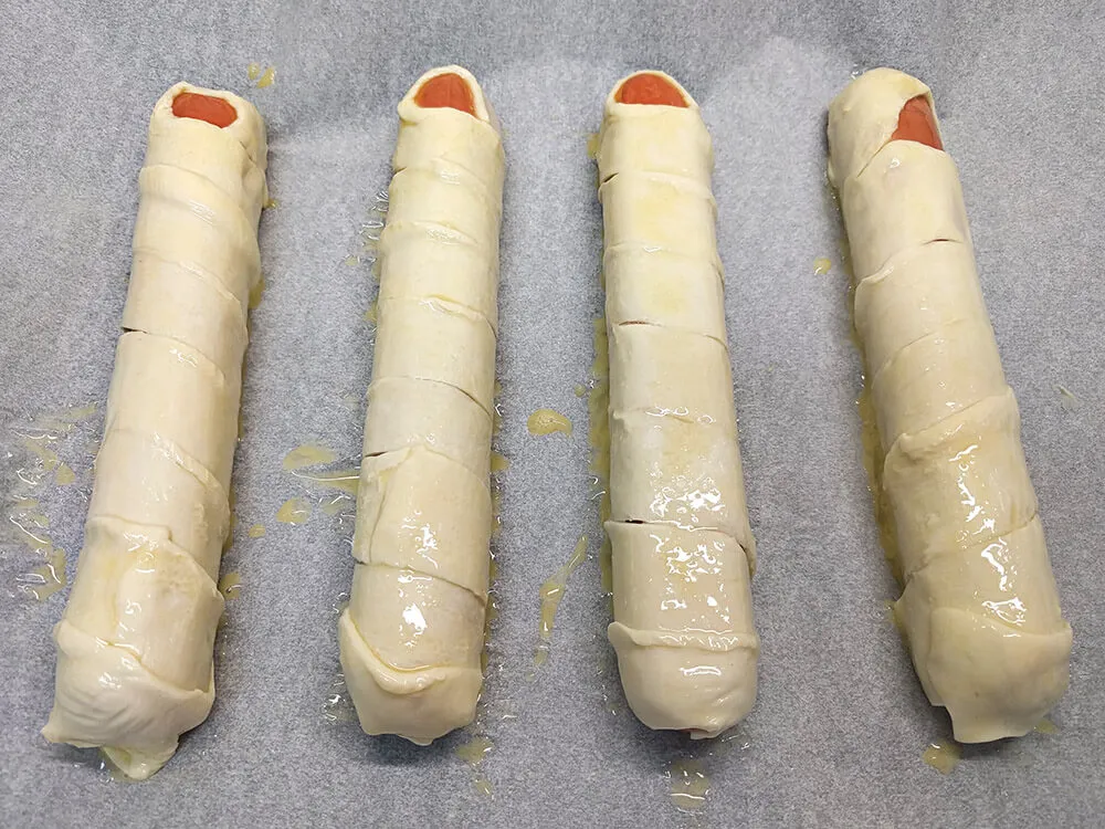 Salchichas envueltas en masa de hojaldre pintadas con huevo batido