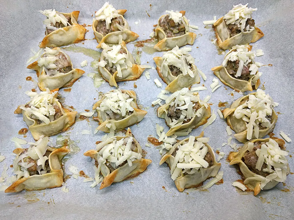 Saquitos horneados con queso rallado listos para gratinar.