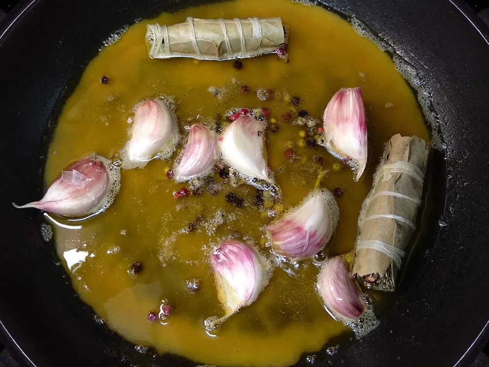 Sartén con aceite de oliva, pimienta, dientes de ajo, laurel y tomillo.