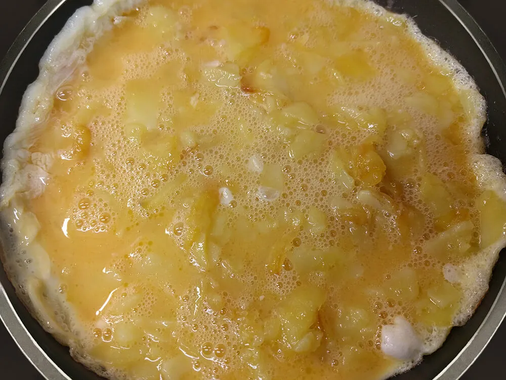 Huevos batidos mezclados con las patatas fritas cuajándose